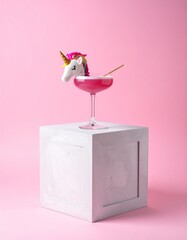Minimalistic composition with a unicorn themed cocktail in a martini glass, placed on a modern concrete cube, set against a soft pink background.