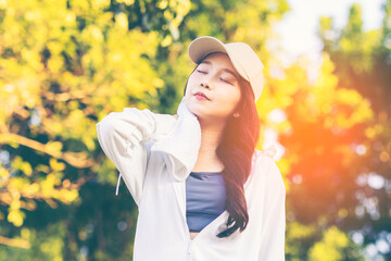 Asian woman wearing wireless headphones, smiling while relaxing in a park after workout and stretching, enjoying music and peaceful outdoor moment of contentment and well-being. 