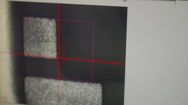 Microscope close-up of an integrated circuit die with red crosshair overlay, revealing intricate silicon microchip layout and probe contacts during semiconductor inspection