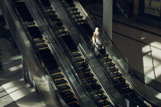 Three escalators descending in atrium, rails reflecting light and casting grid shadows, copy space