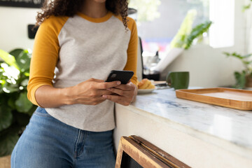 Leaning on marble bar in cafe, African American woman focusing on smartphone near mug and pastry