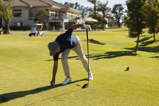 Mature male golfer bending over placing ball on tee while holding driver on tee box
