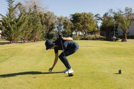 Senior female golfer in sportswear bending forward placing ball on tee holding club on tee box