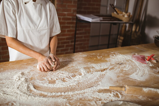 Korean female chef kneading dough on wooden countertop in bakery with rolling pin, copy space