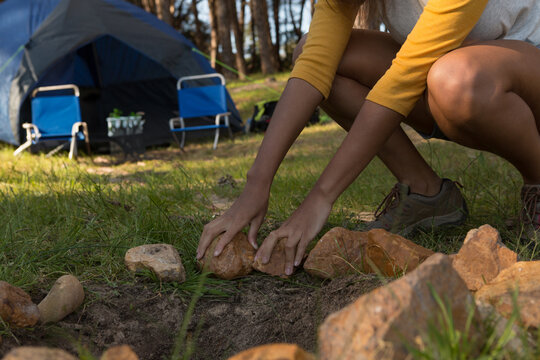 African American woman crouching and arranging stones near dome tent and chairs at camp, copy space