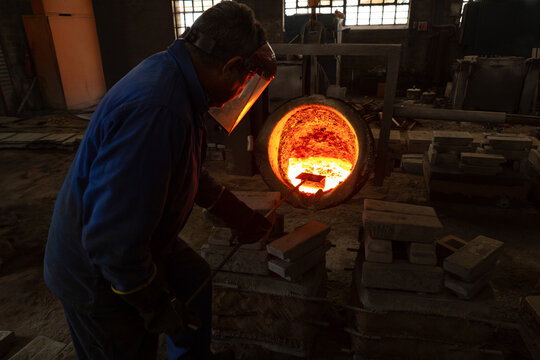 African American man leaning into furnace at foundry stirring molten metal with rod, copy space