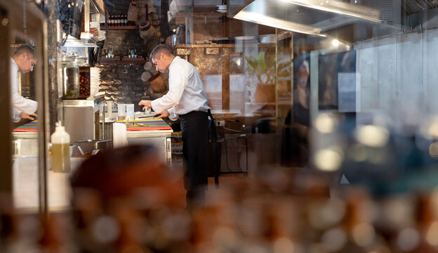 Male chef wearing apron preparing ingredients on cutting board with knife in restaurant kitchen