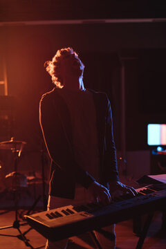 Electronic keyboard emitting orange glow and blue reflection in dim rehearsal room with drum set