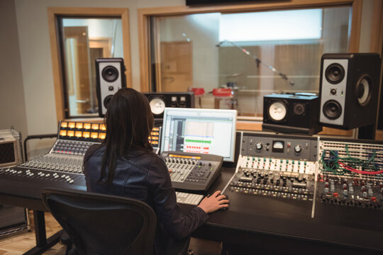 Asian woman wearing jacket operating mixing console and monitoring waveforms in recording studio