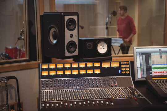 Male vocalist singing into mic holding tambourine while mixing console with VU meters lit in studio