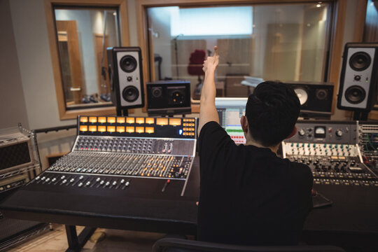 Asian man adjusting faders on mixing console in studio control room with computer screen