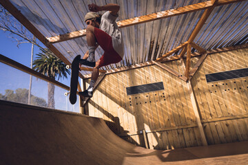 Male skateboarder launching on skateboard off wooden quarter pipe ramp under corrugated roof beams