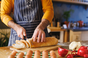 Man in striped apron slicing bread on board at kitchen counter with eggs and measuring cups