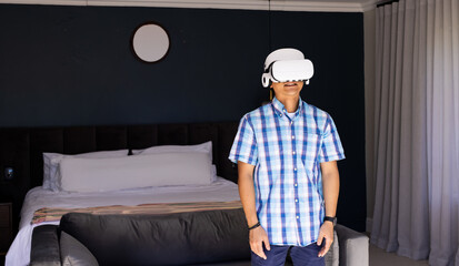 Asian teenage boy wearing VR headset immersing in simulation in bedroom near clock, copy space