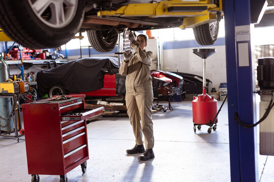 Female auto mechanic in repair garage working under vehicle on hydraulic lift using socket wrench