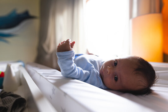Infant boy lying on star-patterned changing pad at softly lit nursery, gazing toward camera