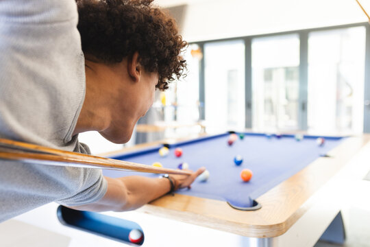 African American man leaning over pool table at home lining up shot with cue, copy space