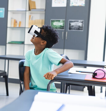 African American child wearing virtual reality headset leaning back in chair in classroom at desk