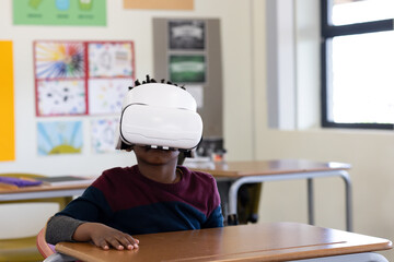 African American boy wearing white VR headset exploring lesson at desk in classroom with supplies