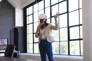 Woman wearing light-colored blazer and jeans interacting with VR headset in modern office