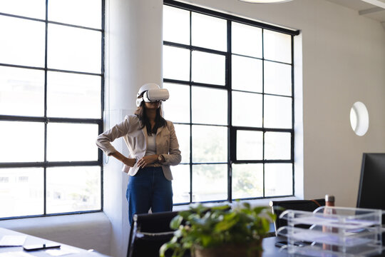 Business woman wearing VR headset and standing at office desk with plant organizer laptop