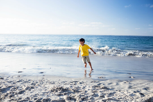 Shallow water splashing over wet sand at shoreline with gentle waves breaking under blue sky