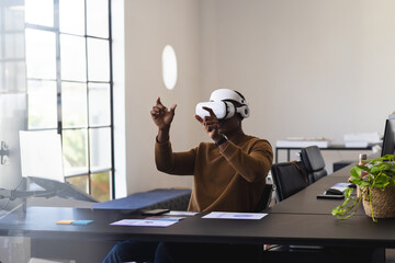 African American man wearing VR headset interacting with interface at office desk with papers phone