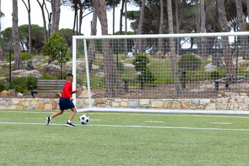 Male child kicking soccer ball toward white goal net on green artificial turf field, copy space