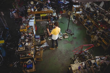 Adult male mechanic adjusting bicycle on repair stand in garage workshop filled with spare parts