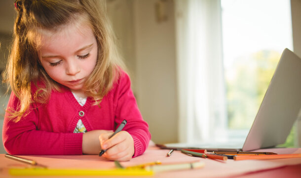Female child drawing with black pen and pencils at study table beside open laptop, copy space
