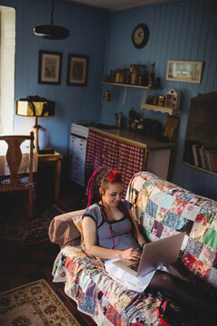 Woman sitting on couch using laptop in cottage lounge with patchwork quilt and stained glass lamp