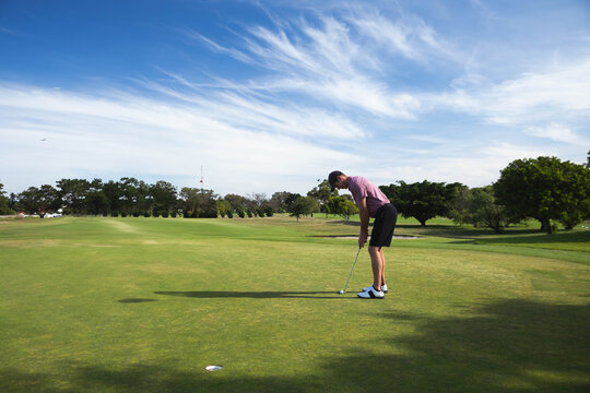 Male golfer leaning on putting green targeting golf ball with putter near hole cup, copy space