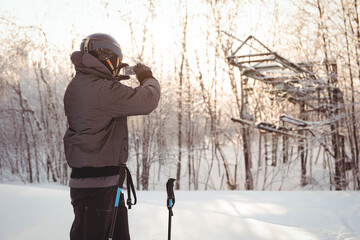 Male skier drinking from water bottle beside poles on trail featuring ski lift frame, copy space