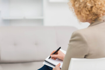 Woman writing notes in spiral-bound notebook with black pen wearing blazer in office, copy space