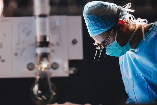 Male surgeon leaning over operating table at surgical suite using loupe headlight, copy space