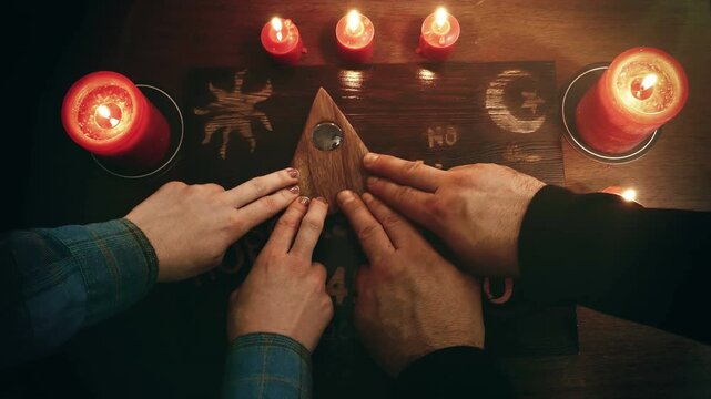 Two people conducting a seance using a homemade talking spirit board, with red candles. Shot from overhead, with some editing for tone. Speaking with the dead through aided by a psychic or medium.