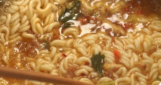 Korean spicy ramyong soup with instant noodles being stirred with chopsticks, close-up footage.