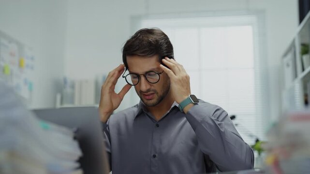 Exhausted worker in a corporate office struggling with the weight of financial reports, feeling the pressure to perform while battling feelings of disappointment.
