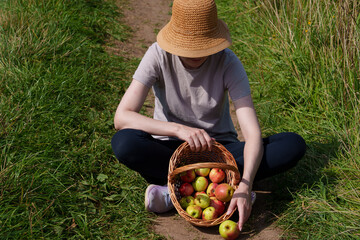 A woman sits cross-legged in the middle of a worn path. Next to her is a basket containing ripe...