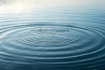 Water ripples outwards in perfect concentric circles across a calm, reflective surface, creating a serene and captivating visual effect under soft, natural light.