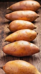 Baked sweet potatoes arranged in a row on a wooden surface. The sweet potatoes are orange and have a smooth texture, ideal for stuffing with cheese.