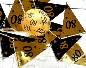 Decorations for a birthday party with black and gold elements placed on a white wooden surface