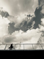 Bicyclist crosses bridge under cloudy sky during afternoon