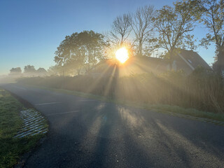 Sun rises behind a house along a foggy road in the early morning