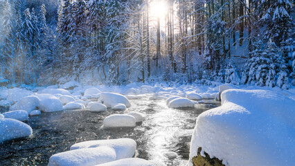 Peaceful winter river flowing through a snow covered forest during gentle snowfall. Soft sunlight...