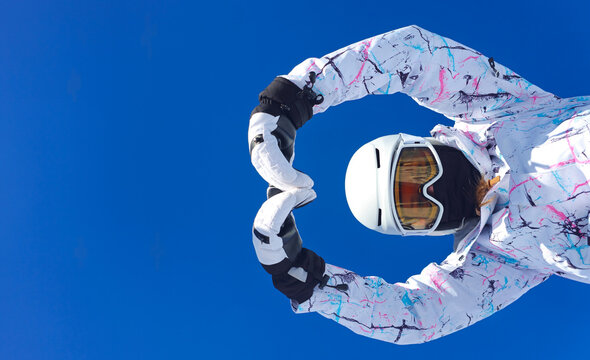 A cheerful skier posing under a bright blue sky, making a heart gesture with hands as a symbol of winter sports enjoyment