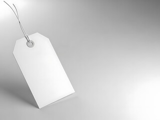 A blank white price tag hanging from a metal string on a gradient gray background