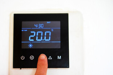 air conditioning, heating, climate change, and energy saving concepts. person turning on the digital heating display and setting it to the desired temperature