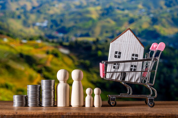 Wooden family figures and stacked coins symbolizing savings and financial growth, with a small house in a shopping cart representing home purchase and real estate investment