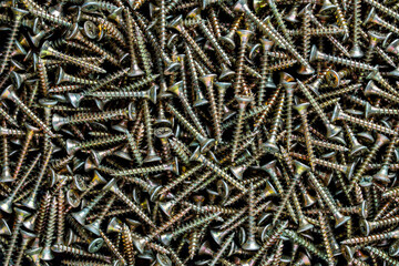 A high-resolution close-up photo of many shiny golden universal self-tapping screws with countersunk heads, piled together in a large messy heap. Perfect for hardware, construction, repair, and DIY pr